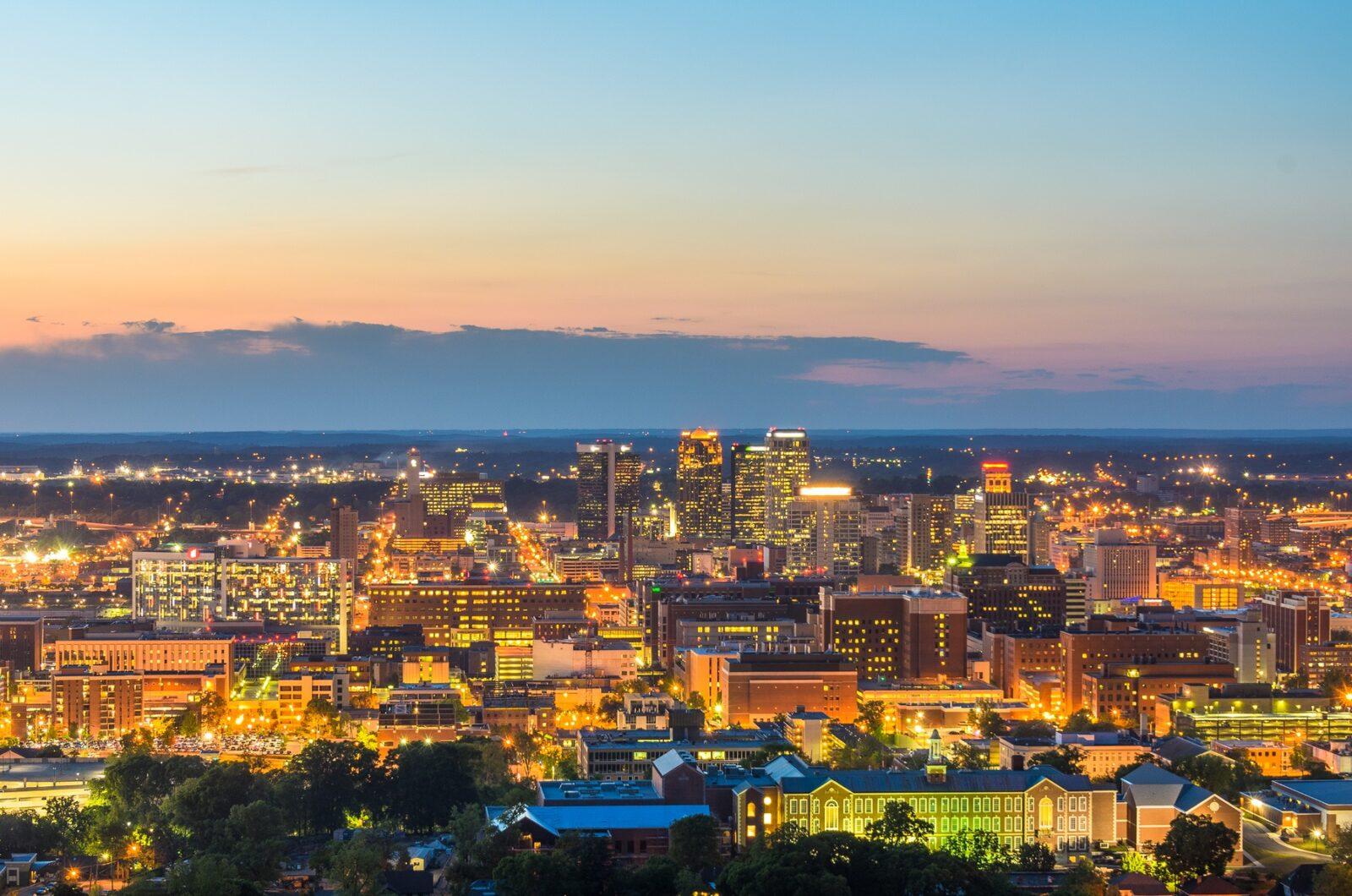 Vibrant cityscape of Alabama at dusk, featuring illuminated skyscrapers, busy streets, and a major highway—representing smooth and reliable car shipping in Alabama for hassle-free vehicle transport.
